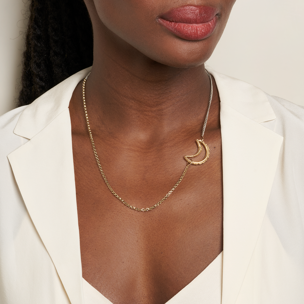 Close up of woman's decolletage wearing long gold and silver two tone chain necklace with moon charm on the right side